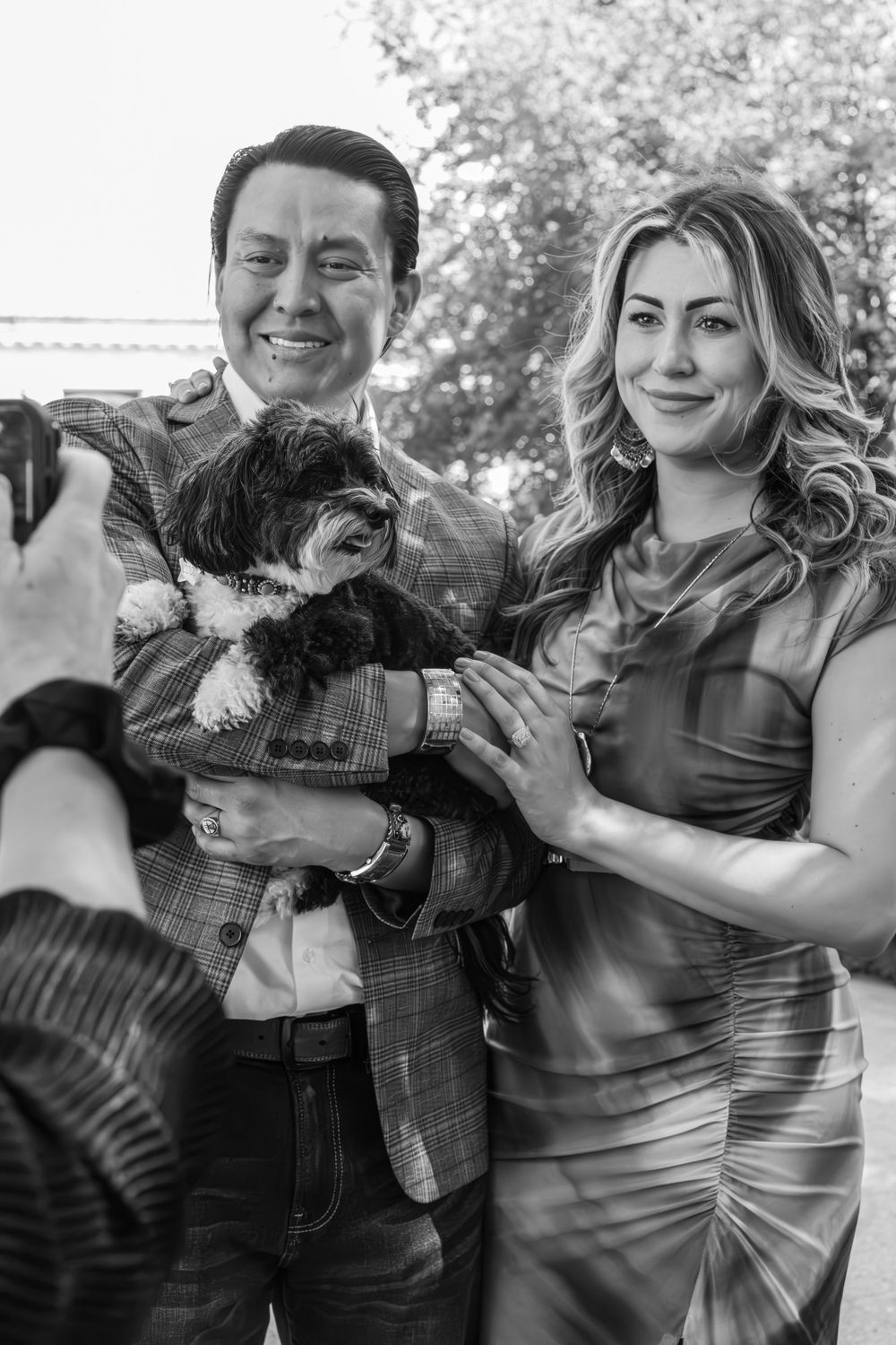 A joyful couple poses with their small dog in a series of black and white outdoor photos.