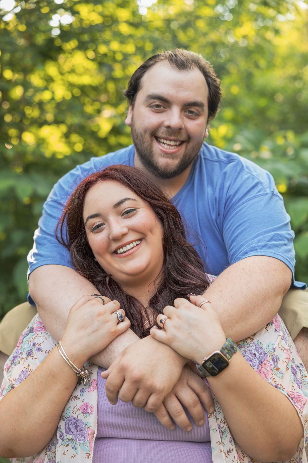 A joyful couple embraces outdoors with sunlit trees in the background.