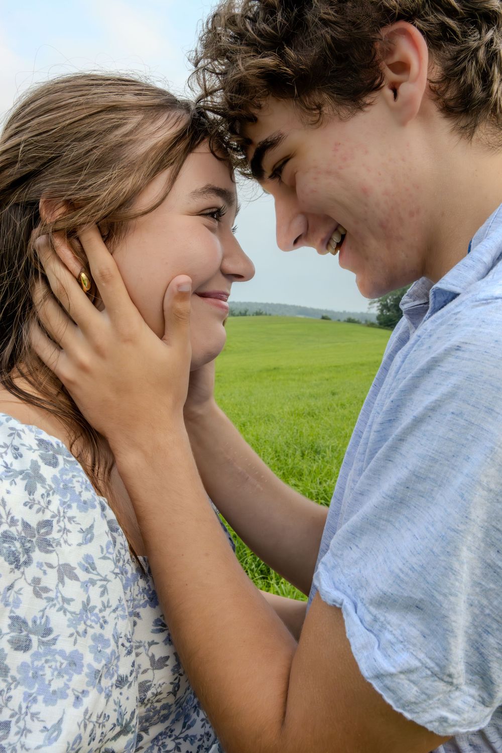 A romantic couple shares an intimate moment in a green meadow field on a sunny day.