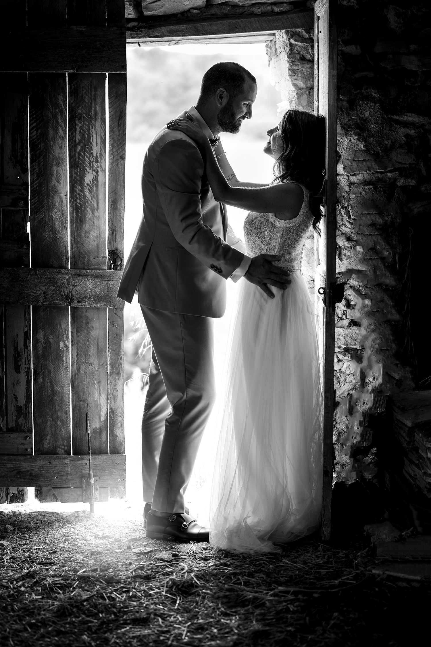 Silhouetted couple in doorway sharing intimate moment in rustic barn setting.