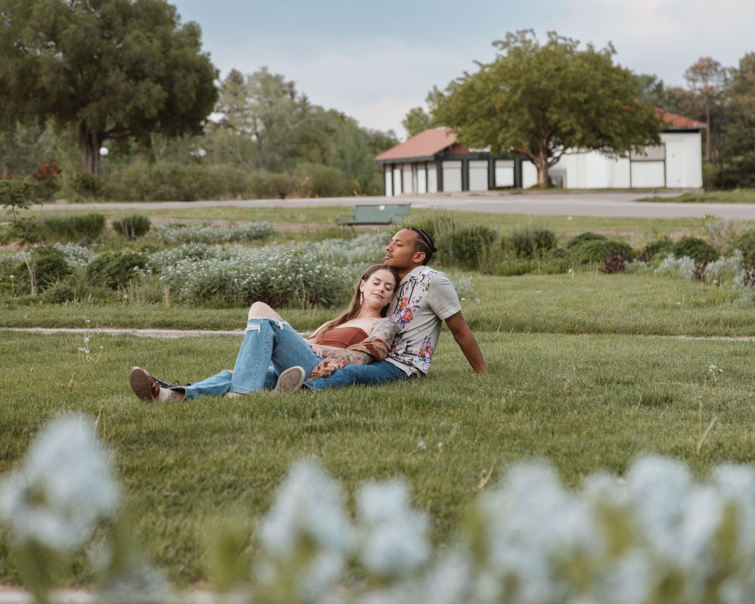 Couple relaxing together on grass with white building in background.