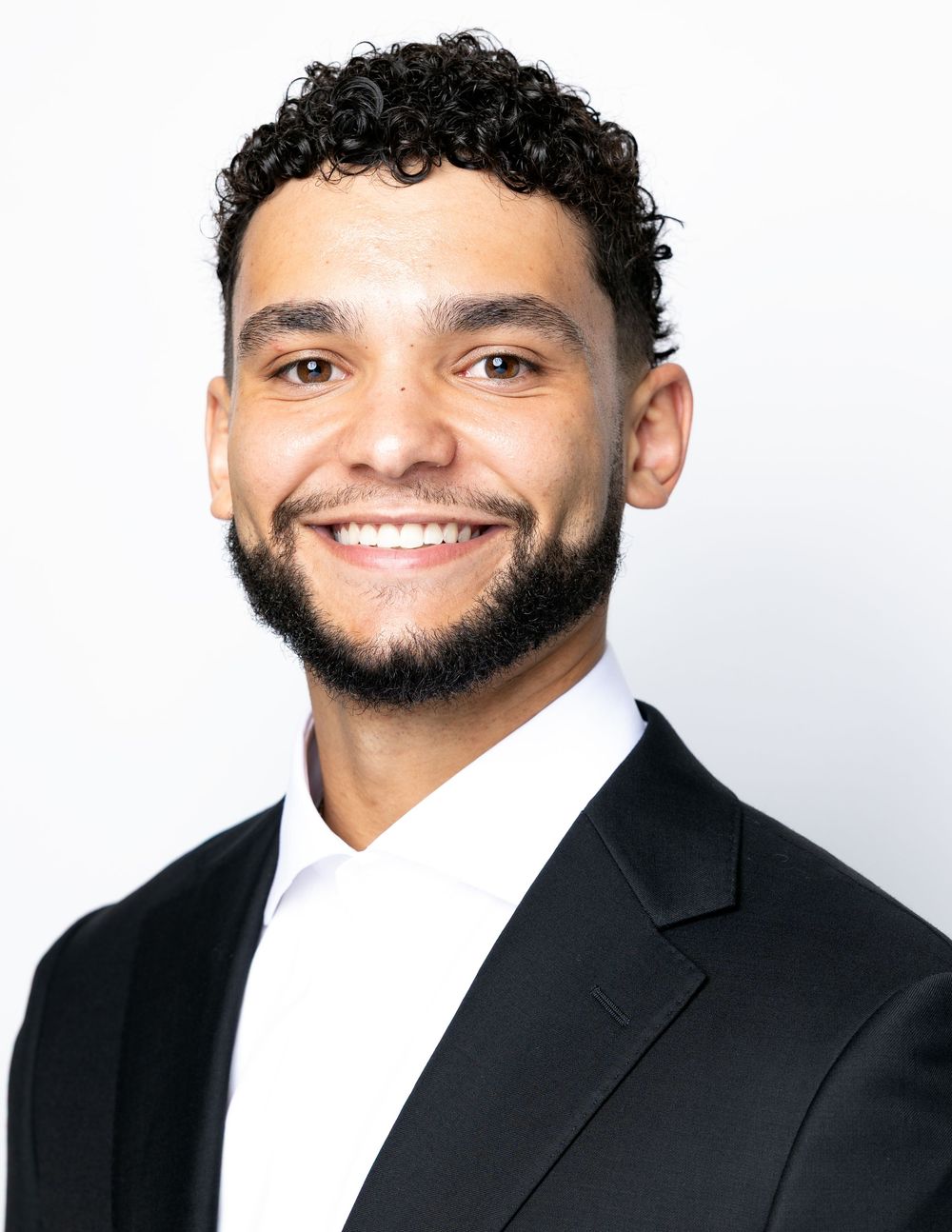 Professional headshot of person in black suit against light background smiling warmly at camera.