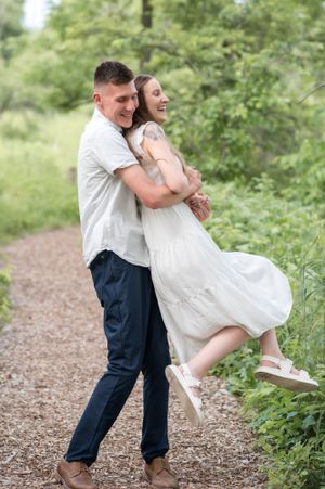 Playful couple dances on a woodland path surrounded by green foliage.