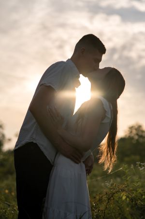 Silhouetted couple shares an intimate moment at sunset in a meadow.