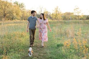 Couple walks through a sunlit field with their dog on a warm autumn day.