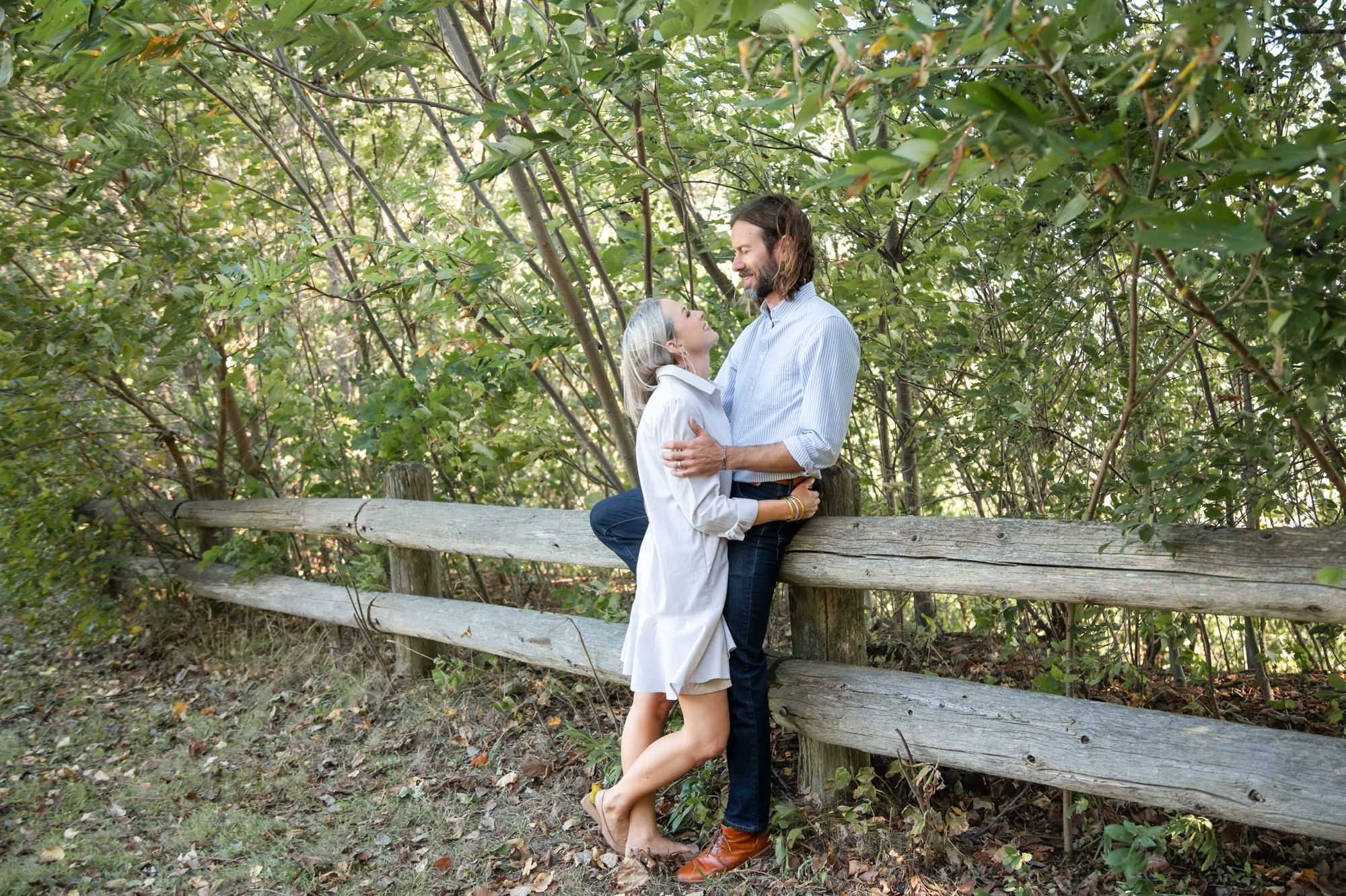 Romantic couple poses against wooden fence in natural outdoor setting.