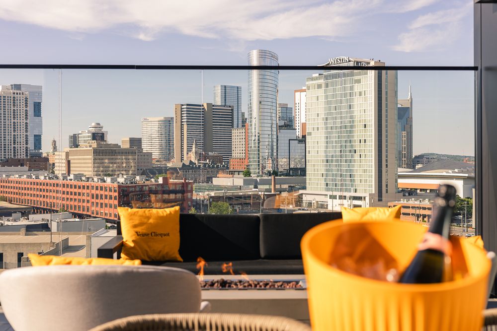 Rooftop bar with Veuve Clicquot champagne bucket, yellow pillows, and stunning city skyline views on a sunny day.