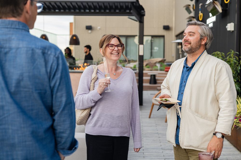 Two smiling adults enjoying casual outdoor conversation at a social gathering, holding drinks and food.