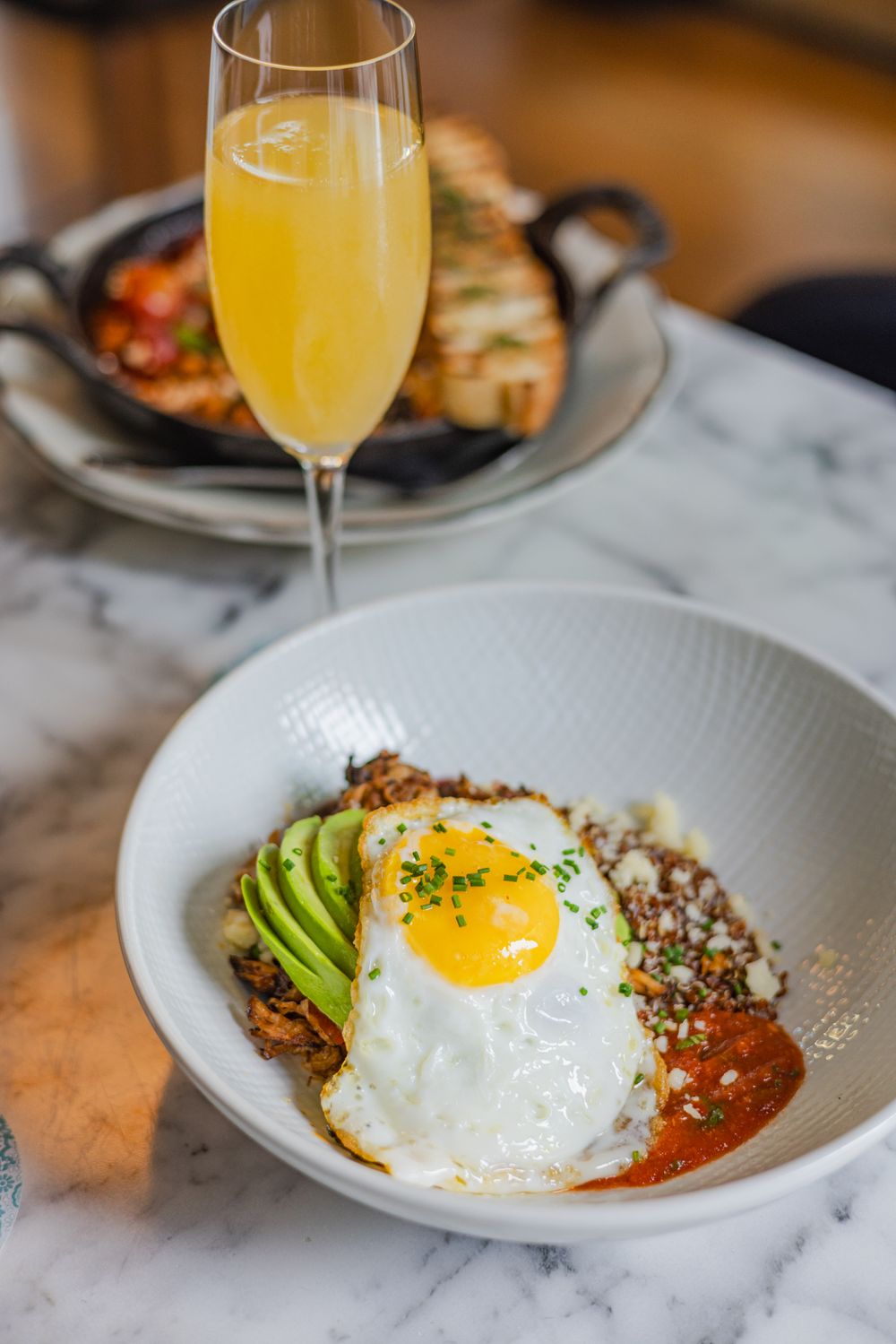 Savory breakfast bowl with sunny side up egg, avocado slices, and quinoa served with a mimosa cocktail.