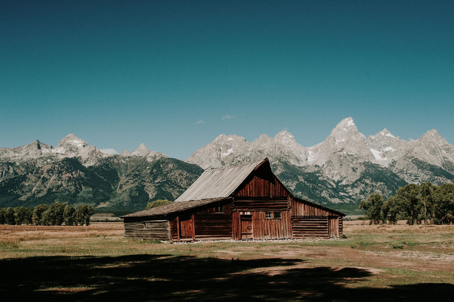 Rustic wooden barn against dramatic mountain backdrop in Grand Teton National Park during golden hour.