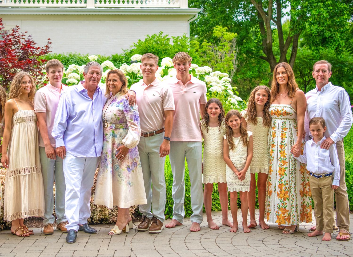 Wedding party members in soft pastel tones and white attire stand together in a row on an outdoor stone path.