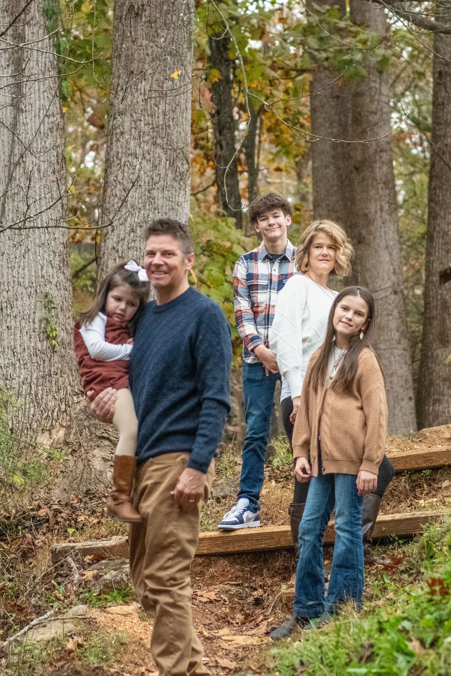 A family group poses on wooden steps among fall trees in a forest.