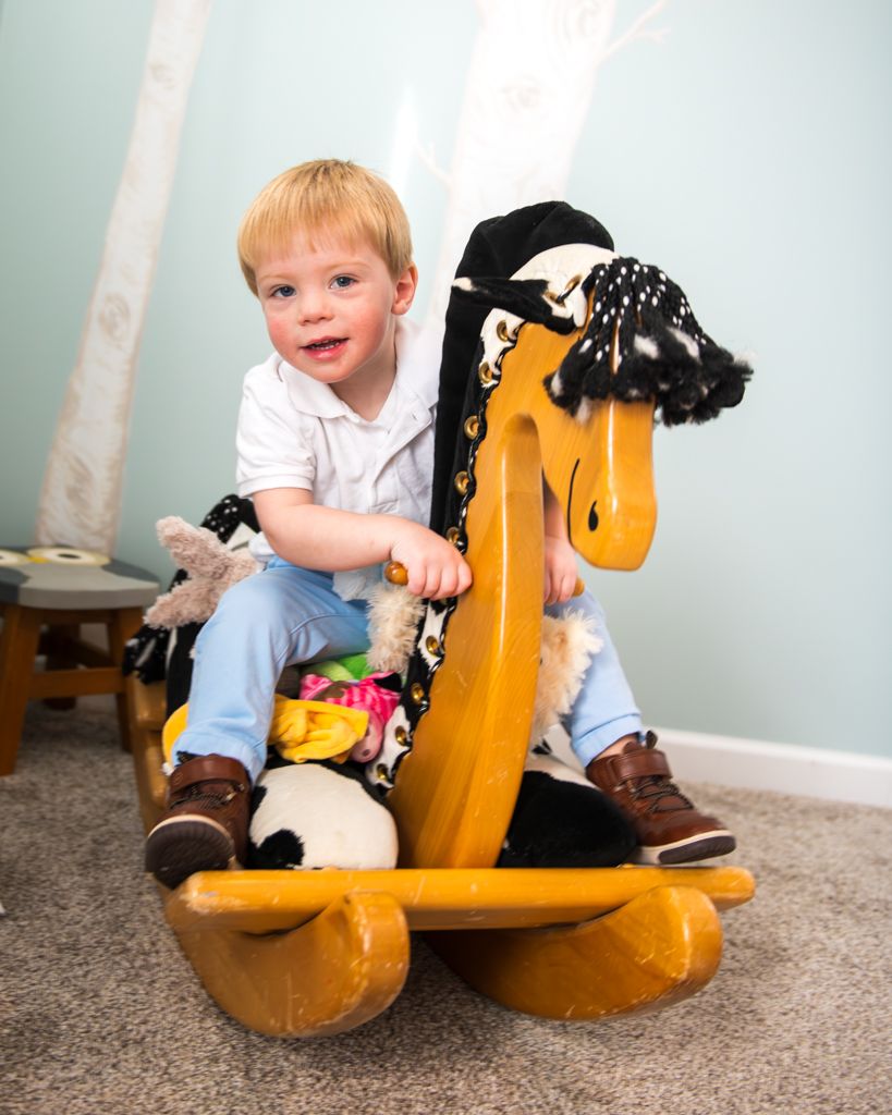 Child rides yellow rocking horse toy while wearing casual outfit.