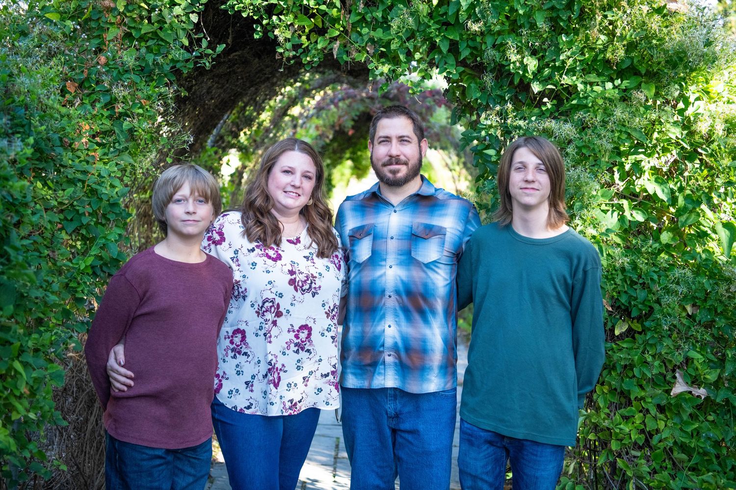 A group of people standing together outdoors in casual clothing with green foliage in the background.
