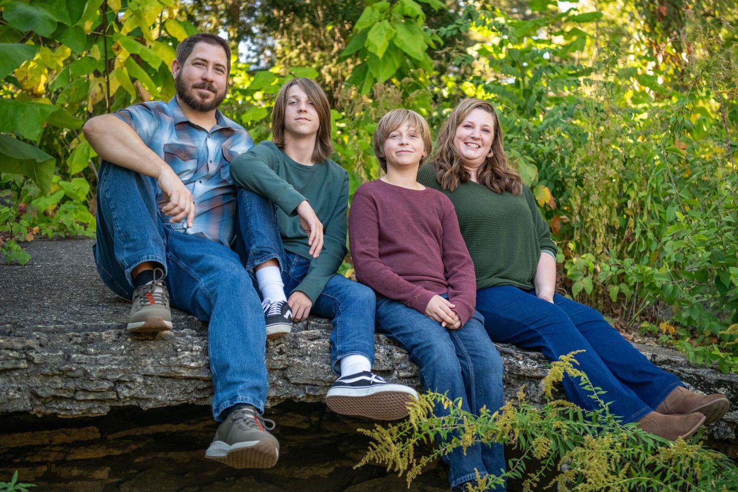 A family sits together on stone steps surrounded by lush green foliage in an outdoor setting.
