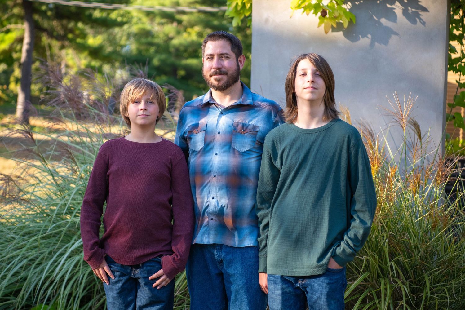 A family stands together outdoors during golden hour in coordinated burgundy and blue outfits for a fall photo session.
