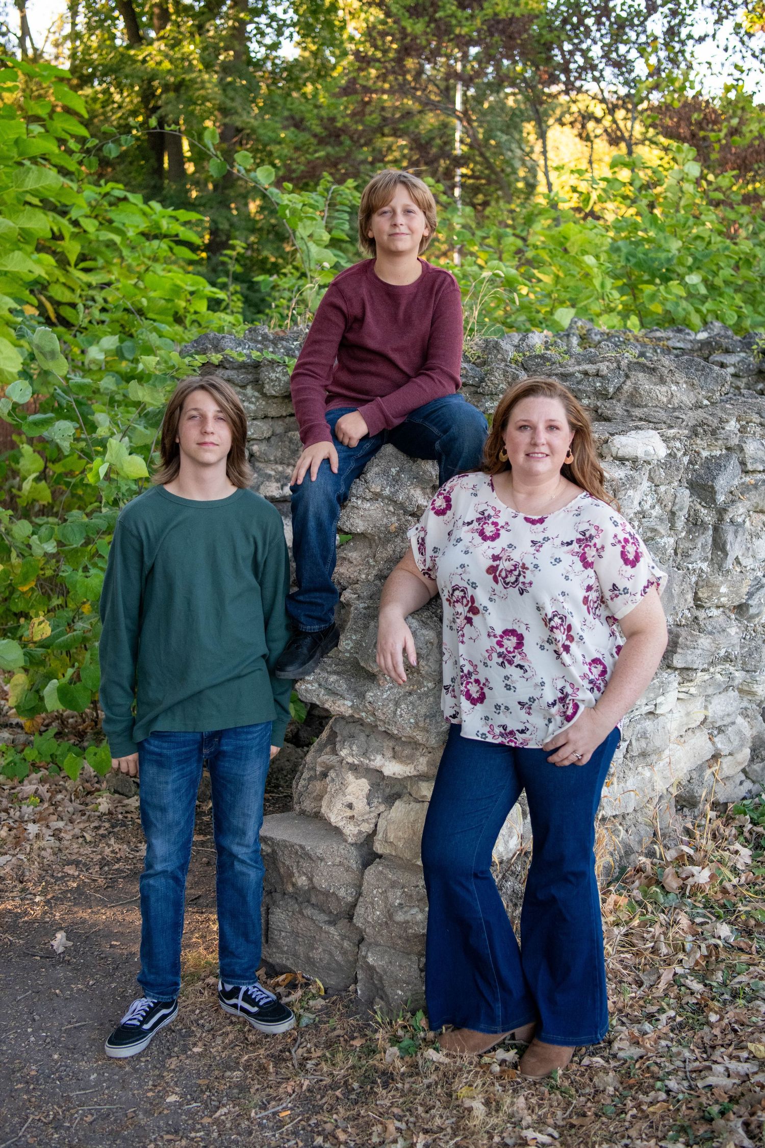 People posing casually against a rustic stone wall in an outdoor garden setting with lush greenery in the background.