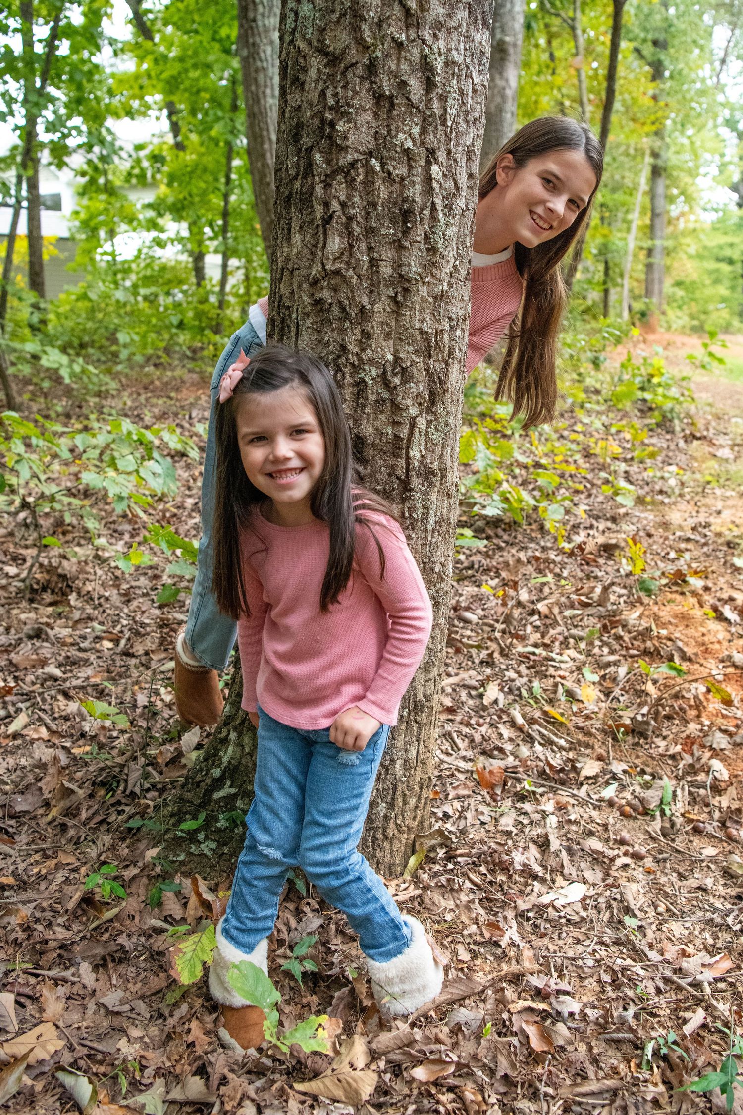 A playful scene among fallen autumn leaves as someone peeks from behind a large tree trunk in the woods.