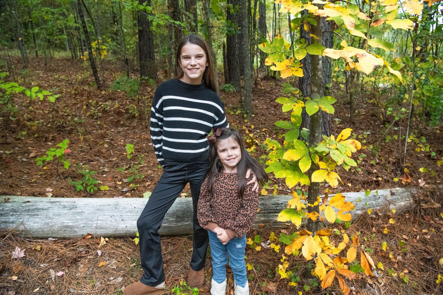 A person in jeans and boots walks through autumn woods with yellow leaves falling from trees in the background.