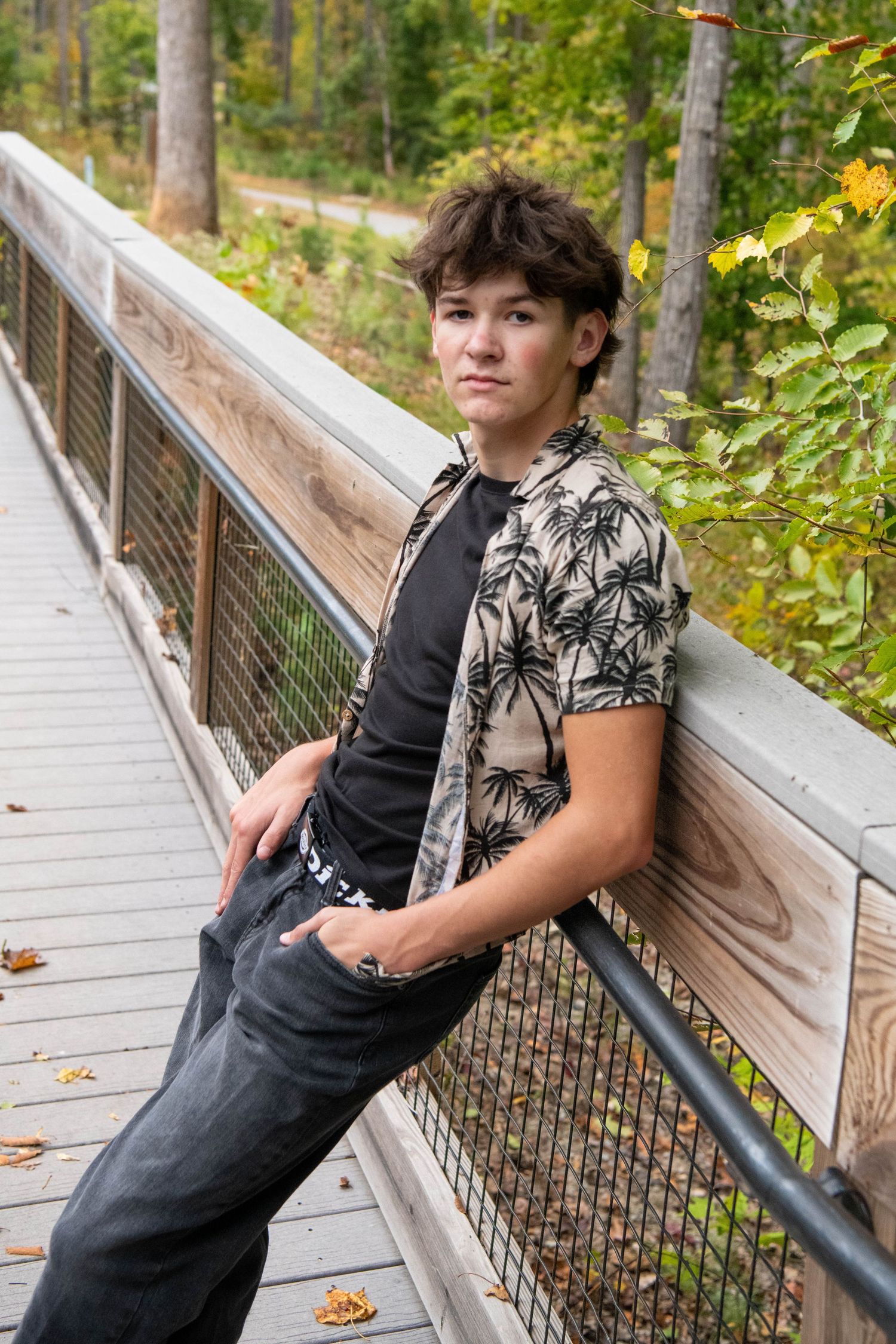 A person in a floral top leans against a wooden railing on an elevated walkway in the forest.