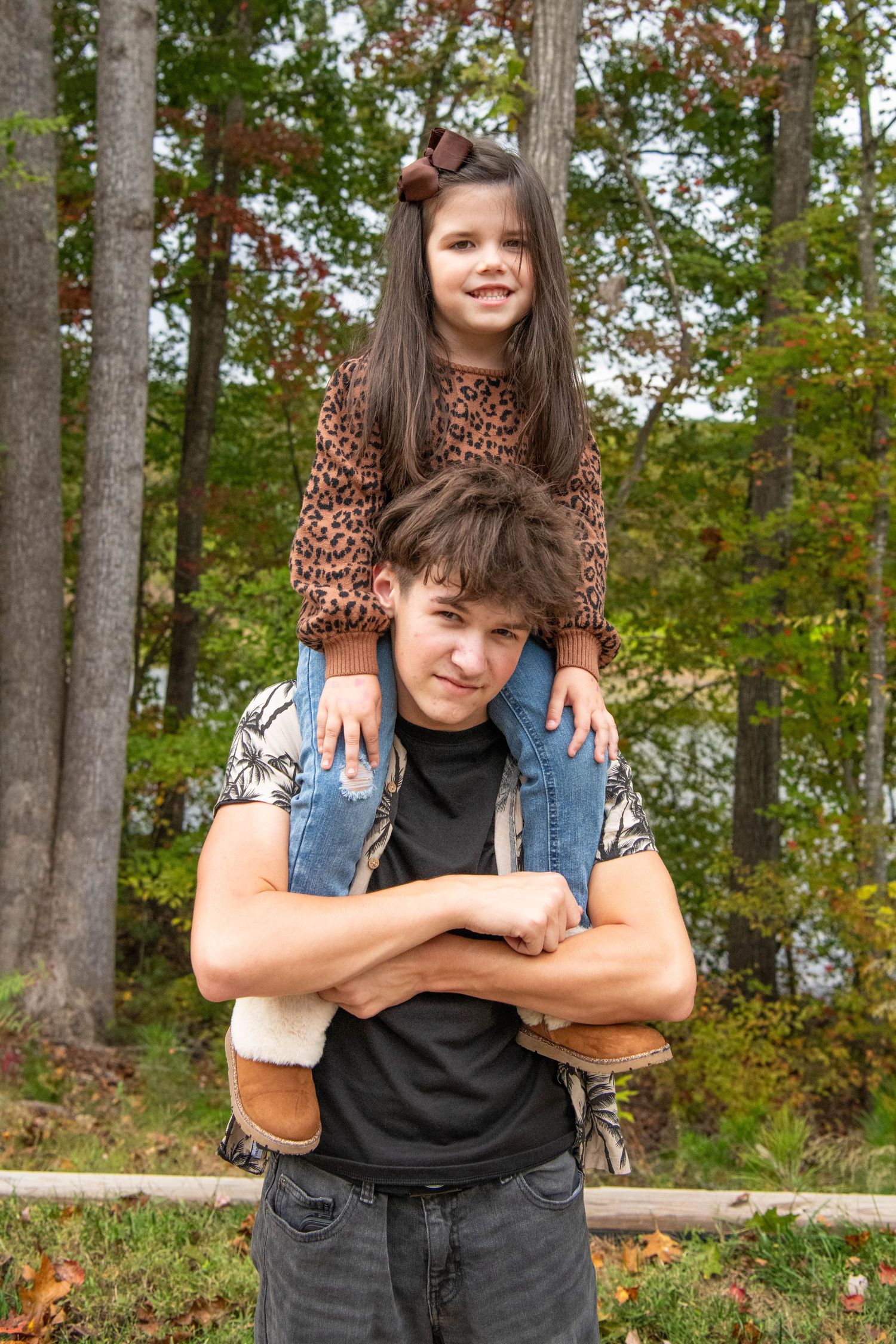 Two people pose together on a wooden bench in a wooded area during autumn.