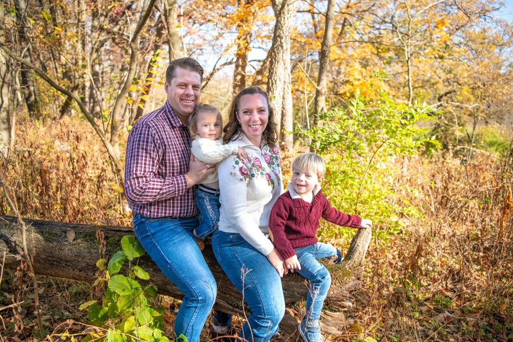 A family poses together on a log in an autumn forest setting.
