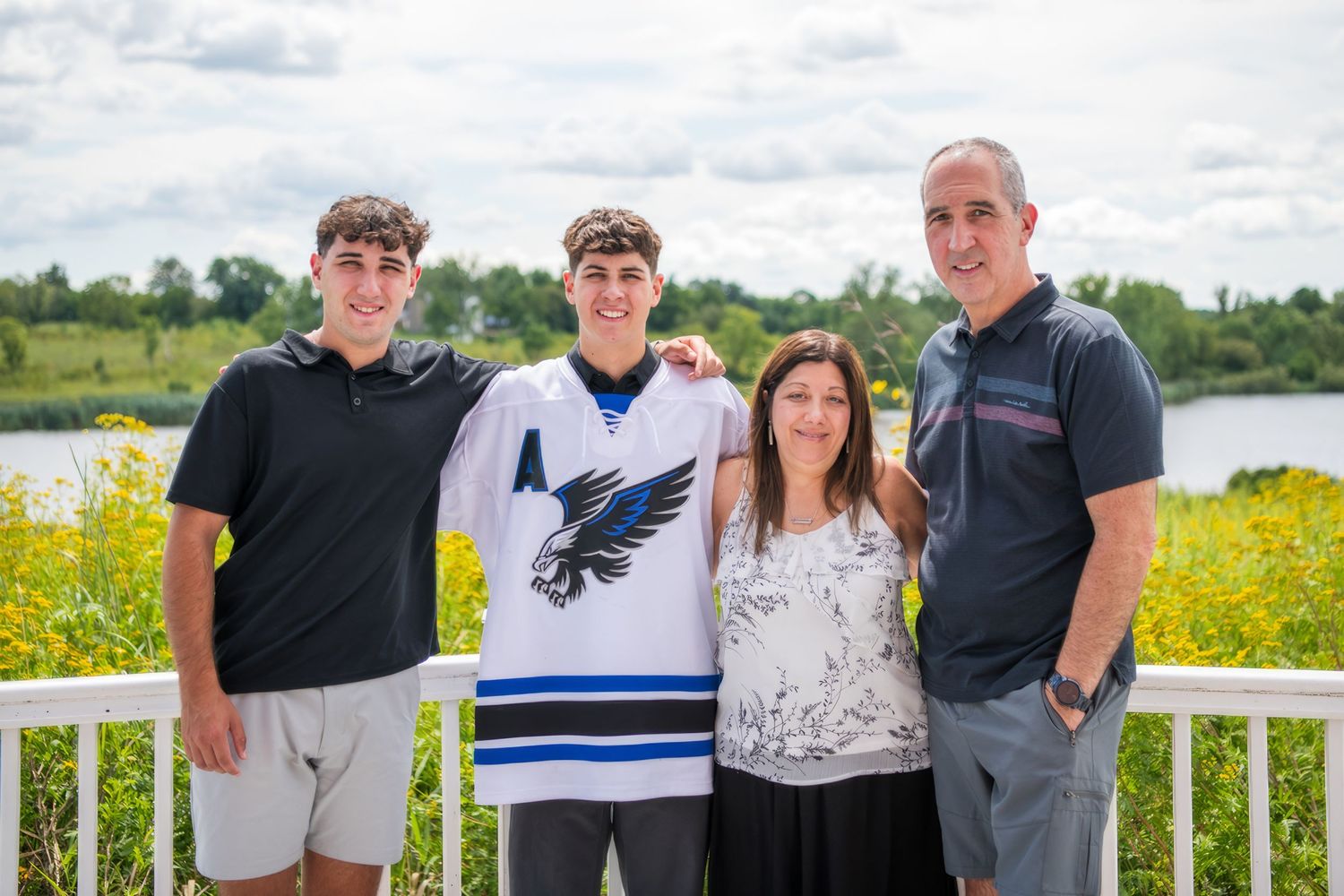 Group photo on a deck overlooking a lake with yellow wildflowers in the background.