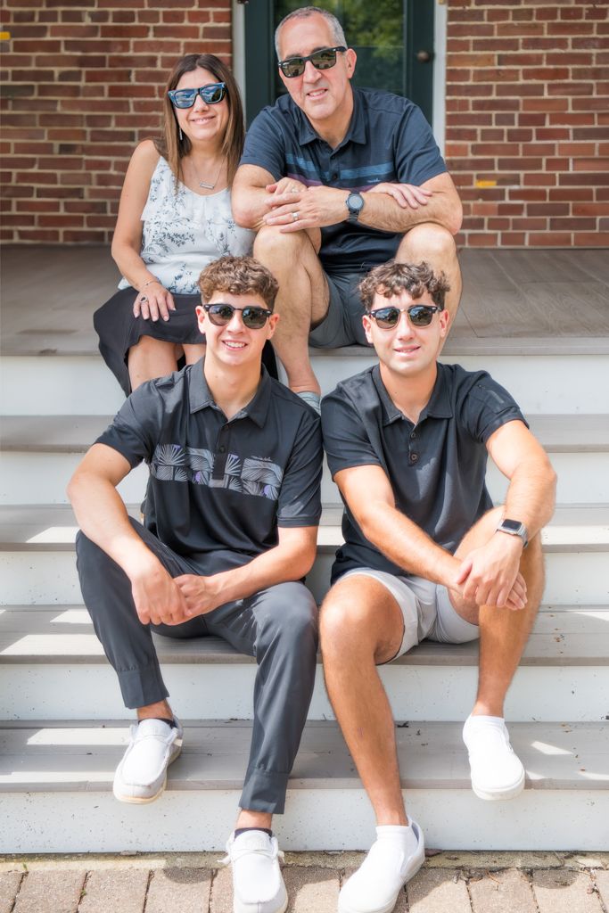 Family gathering on brick porch steps wearing casual summer attire.