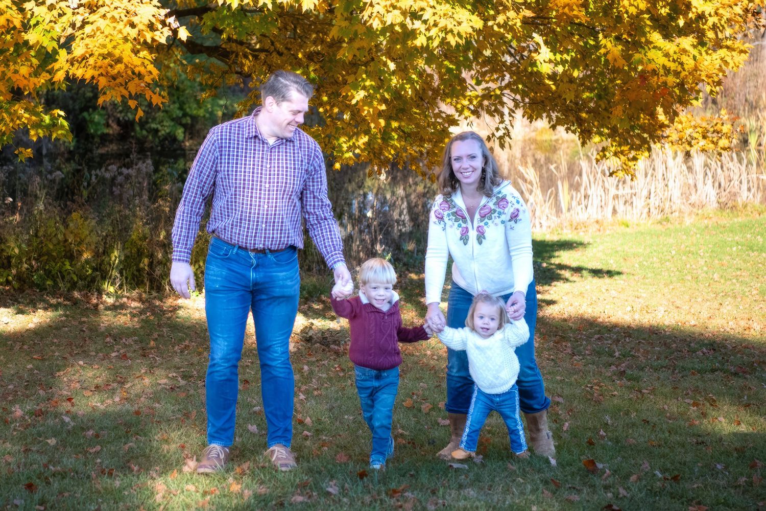 Family standing together outdoors among fall foliage with golden trees in background.