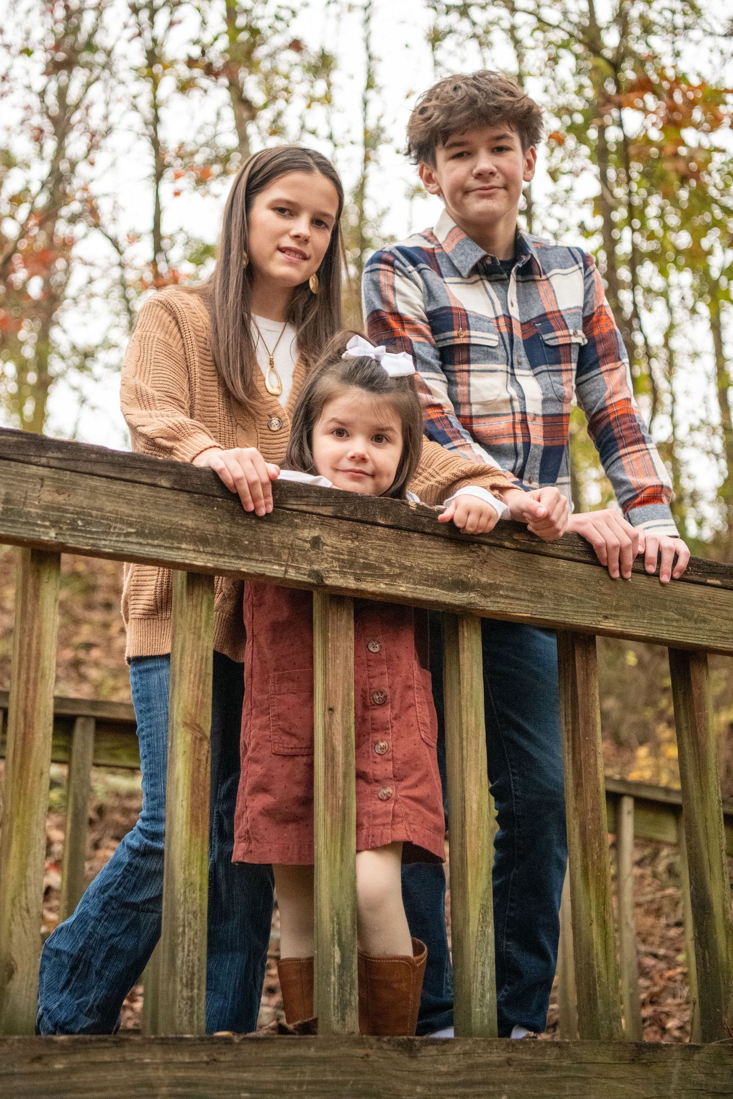 Three people standing together on a wooden deck railing in an autumn forest setting.