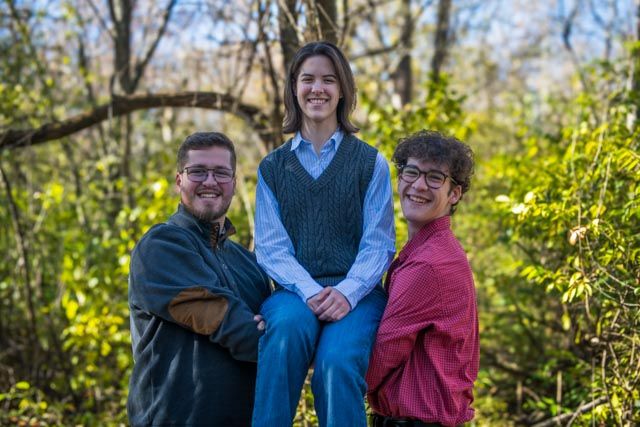 Three people share a joyful moment together outdoors on a sunny day surrounded by greenery.
