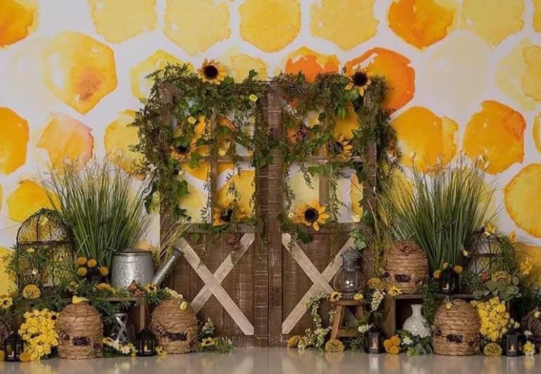 A honeycomb-themed backdrop with rustic wooden decor, sunflowers, and greenery creates a charming garden party setting.
