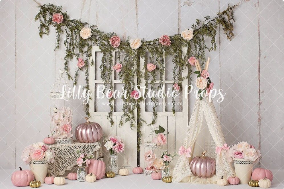 Romantic wedding reception setup with pink pumpkins, floral arrangements and rustic garden decor against white backdrop.