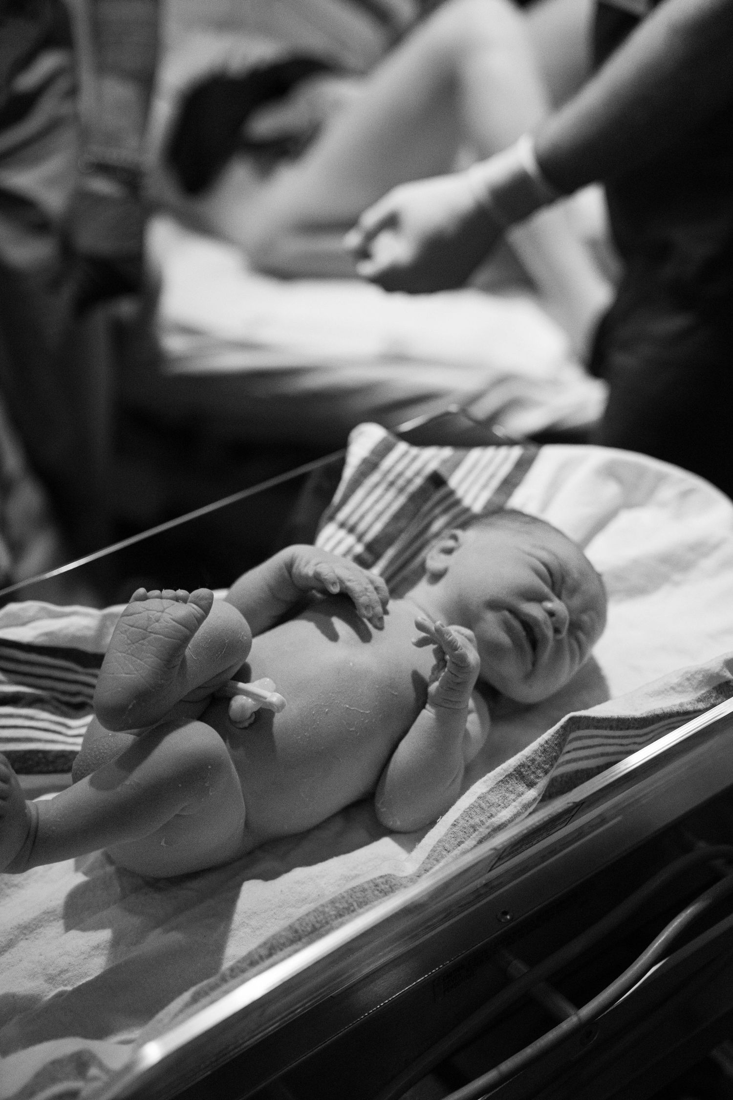 Black and white capture of newborn being measured on medical scale.