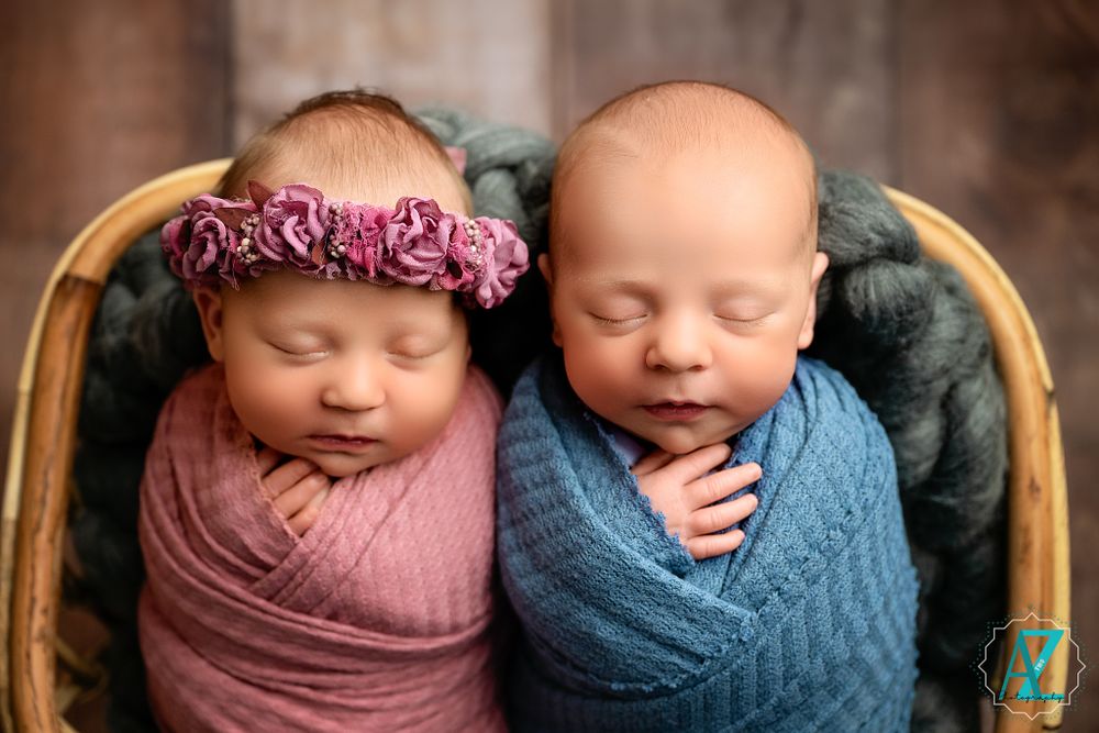 Sleeping twins wrapped in pink and blue swaddles with one wearing floral crown.