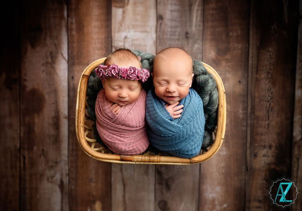 Twin babies in basket with one sleeping in pink wrap and one giggling in blue wrap.