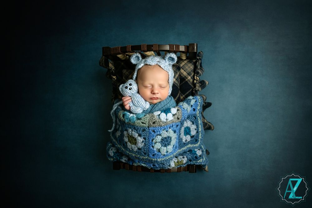 Sleeping newborn wrapped in blue patterned fabric resting in vintage decorated container.