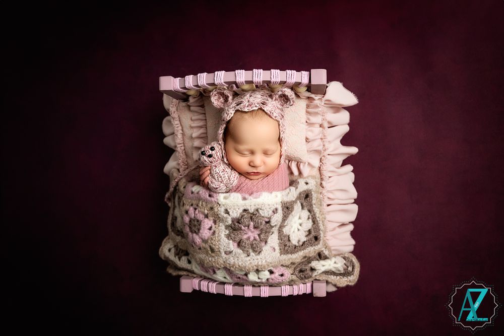 Newborn sleeping in pink floral bedding surrounded by soft ruffled fabric during studio session.