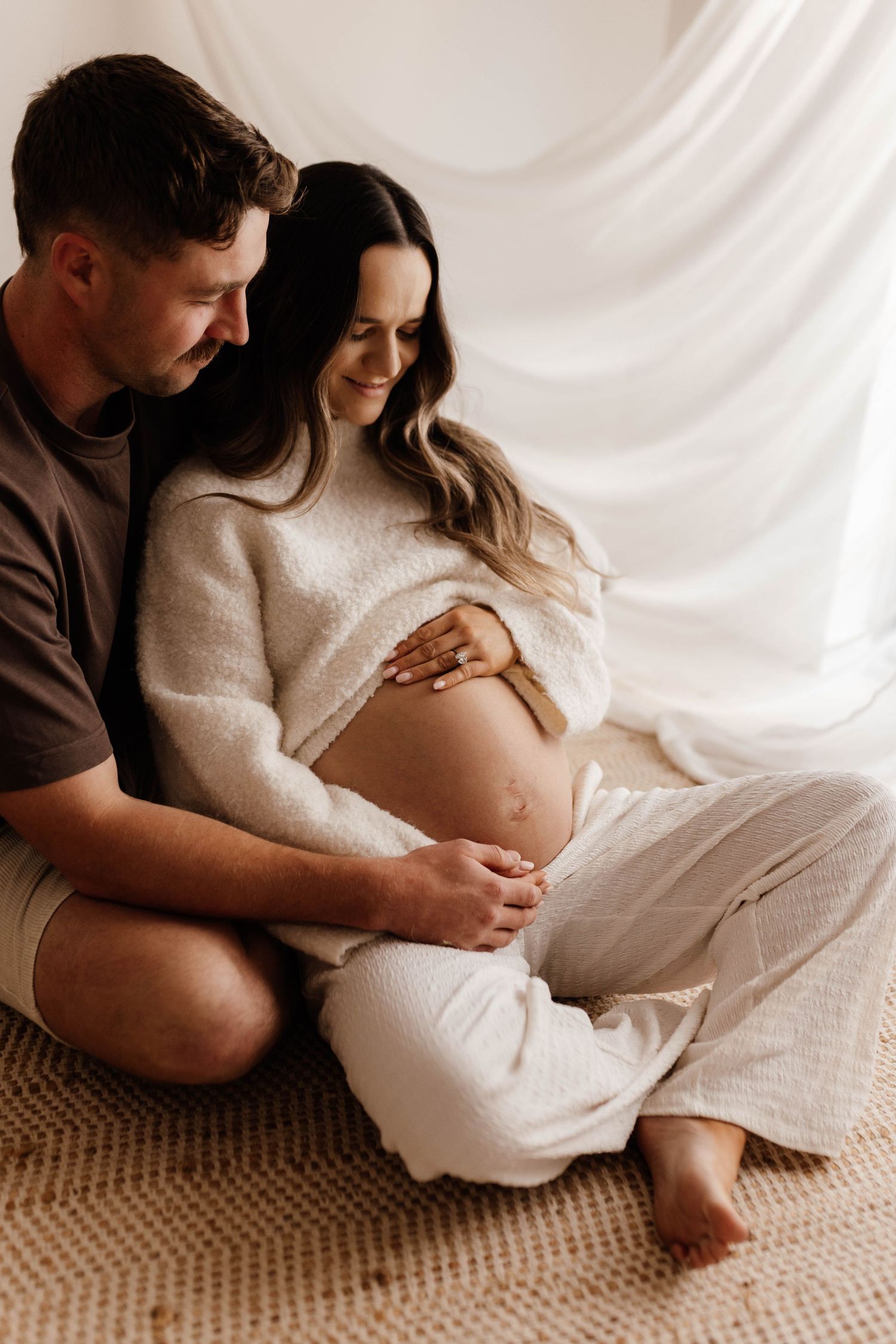Tender family moment captured in soft natural light with baby nestled in white lace.