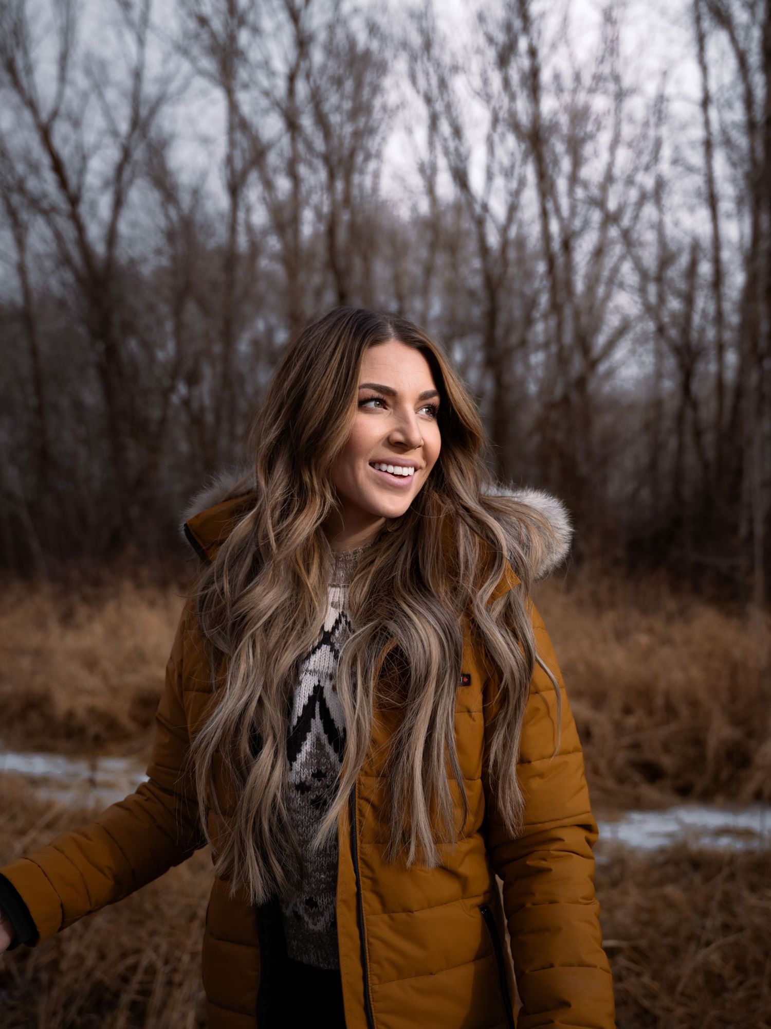 Person in mustard yellow winter coat enjoying a moment in the autumn woods.