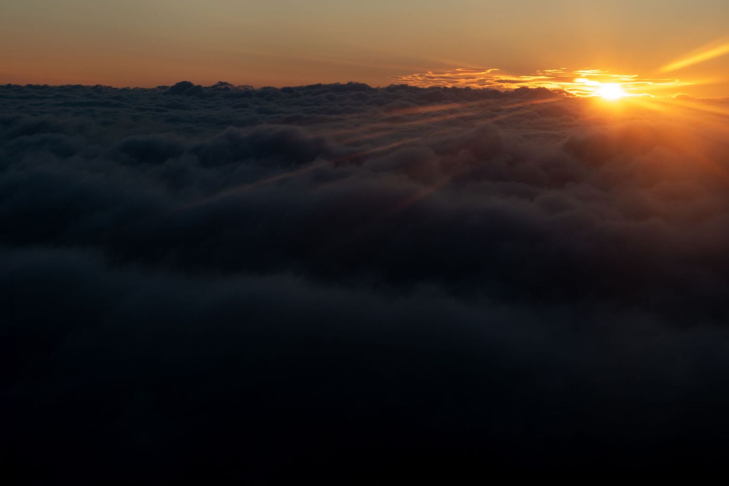 Dramatic sunset over clouds with mountains silhouetted in the distance.