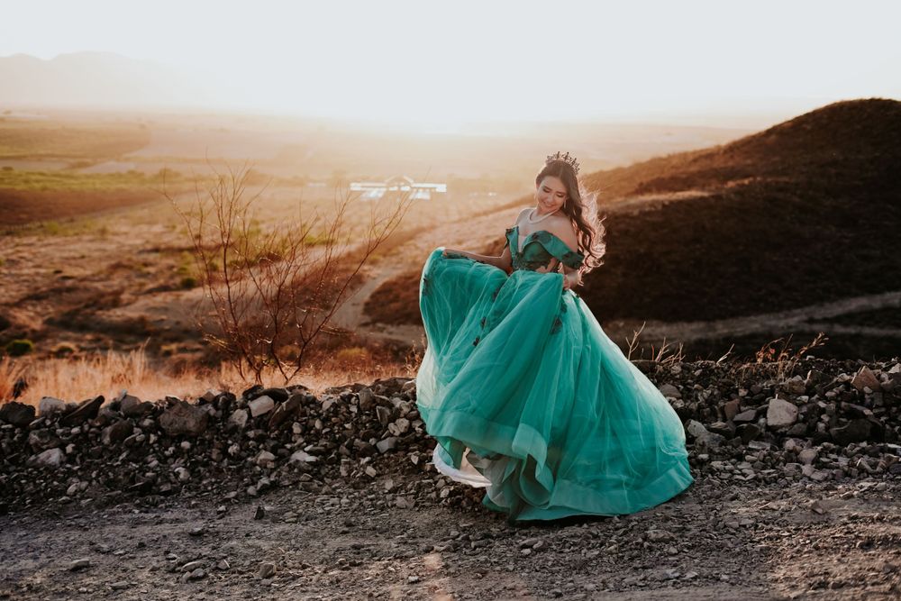 A teal ballgown flows dramatically in the wind against a mountainous landscape.