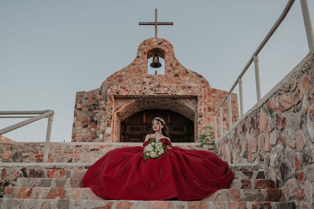 A dramatic red ballgown photographed in front of a rustic stone church with a bell tower.