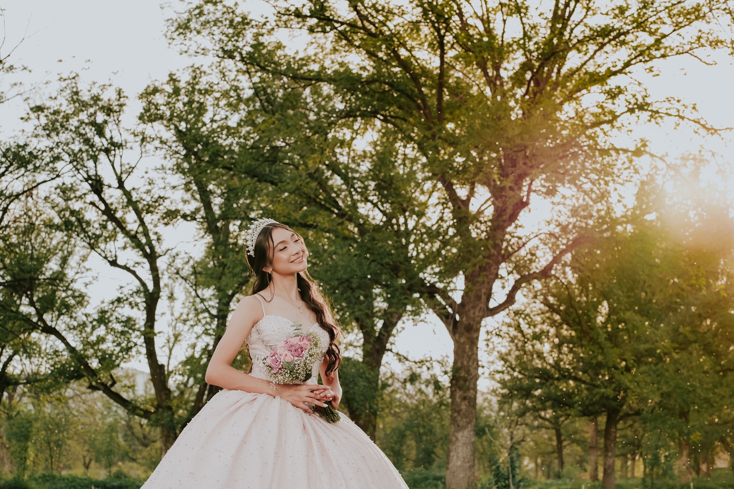 Golden sunset light illuminates a dreamy outdoor wedding photography session amid tall trees and natural greenery.