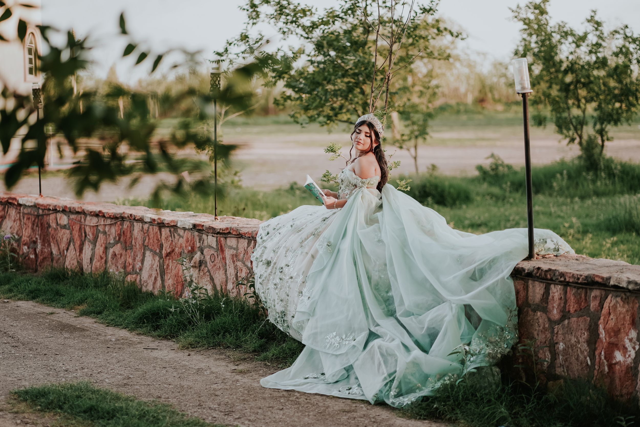 A flowing mint green gown with intricate lace details billows dramatically against a rustic stone wall in an outdoor setting.