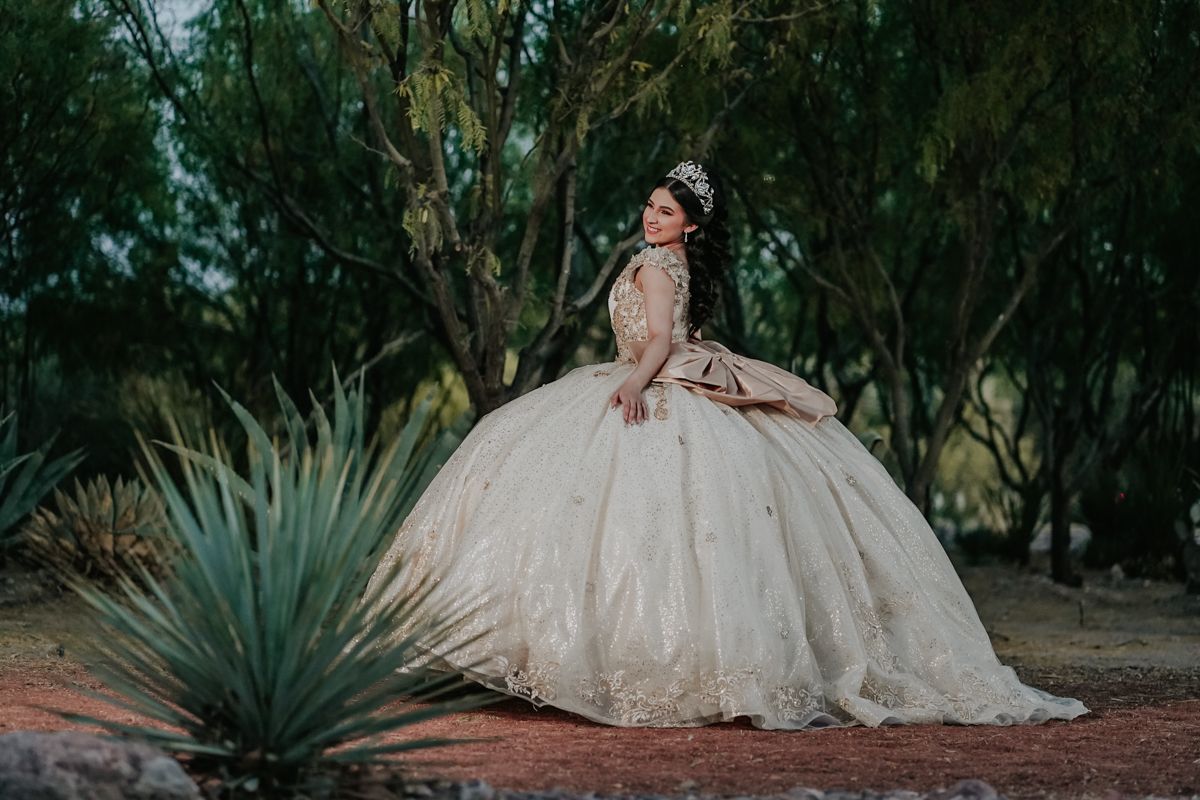 A quinceañera dress glows in the golden light amidst desert plants and trees at sunset.