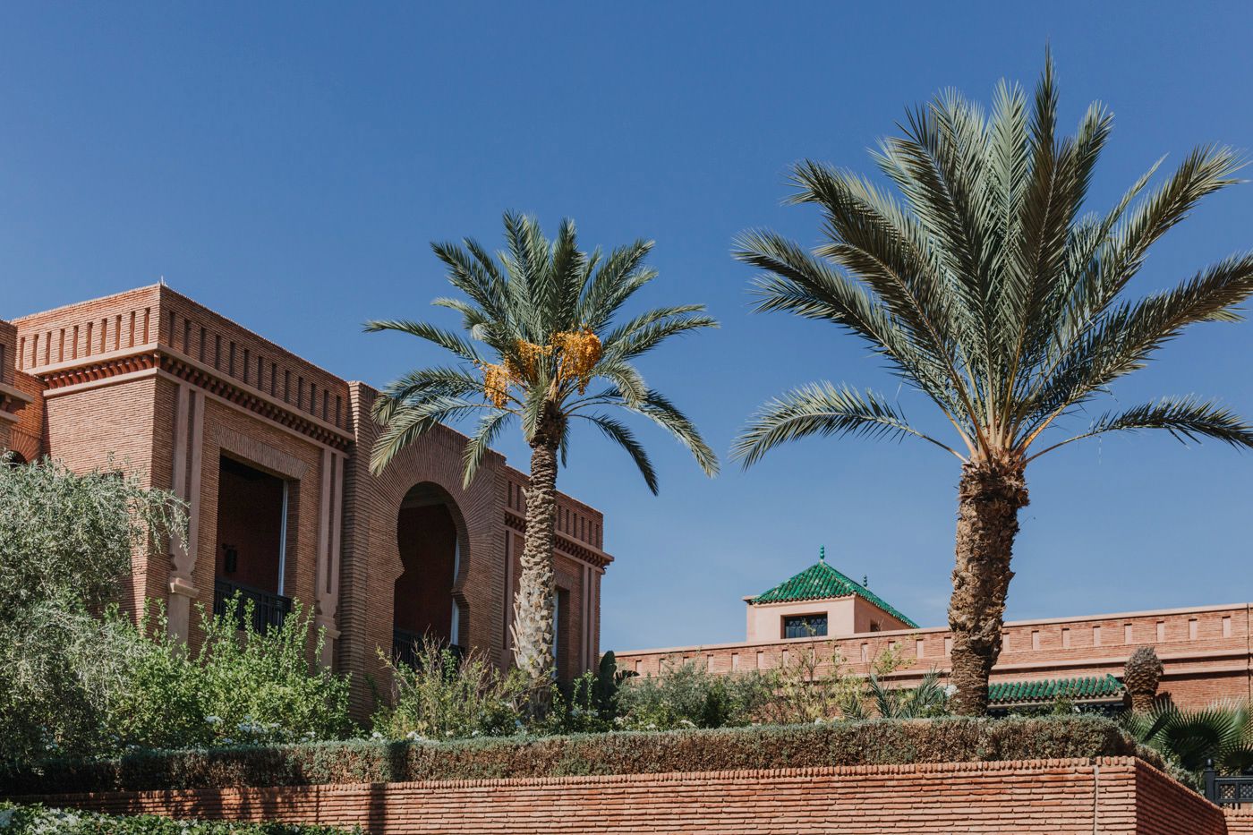 Traditional Moroccan architecture with terracotta walls and palm trees against a bright blue sky.