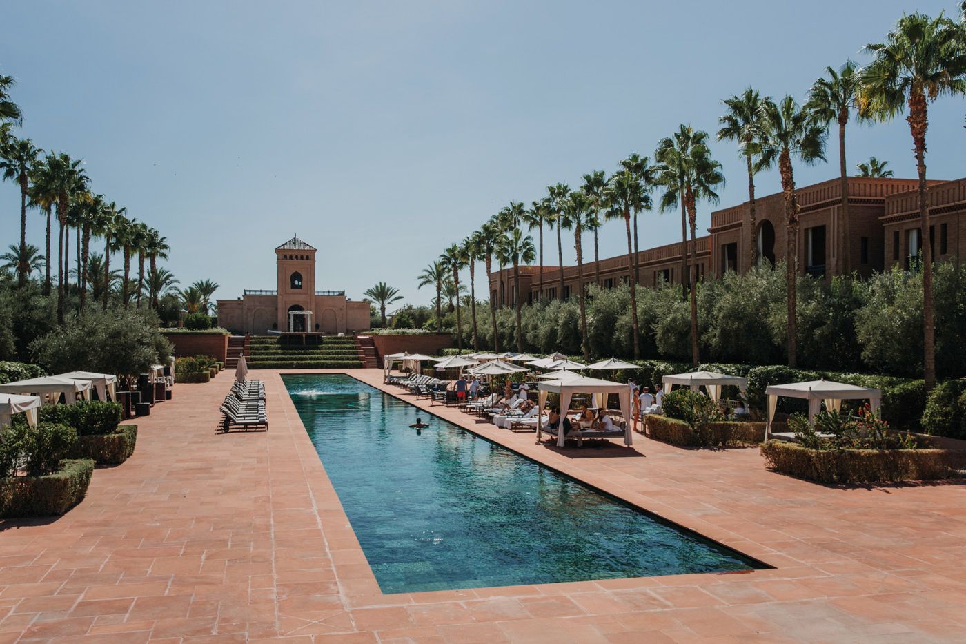 Luxury hotel swimming pool lined with palm trees and sun loungers in Marrakech.