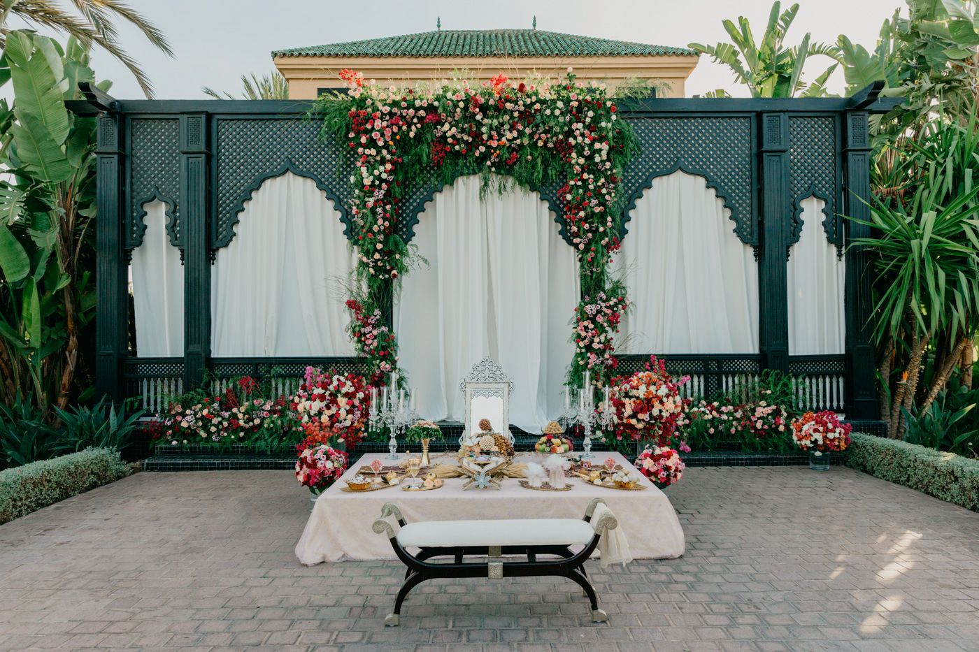 Luxurious wedding backdrop with green panels, floral arches and traditional Moroccan-style seating arrangement.