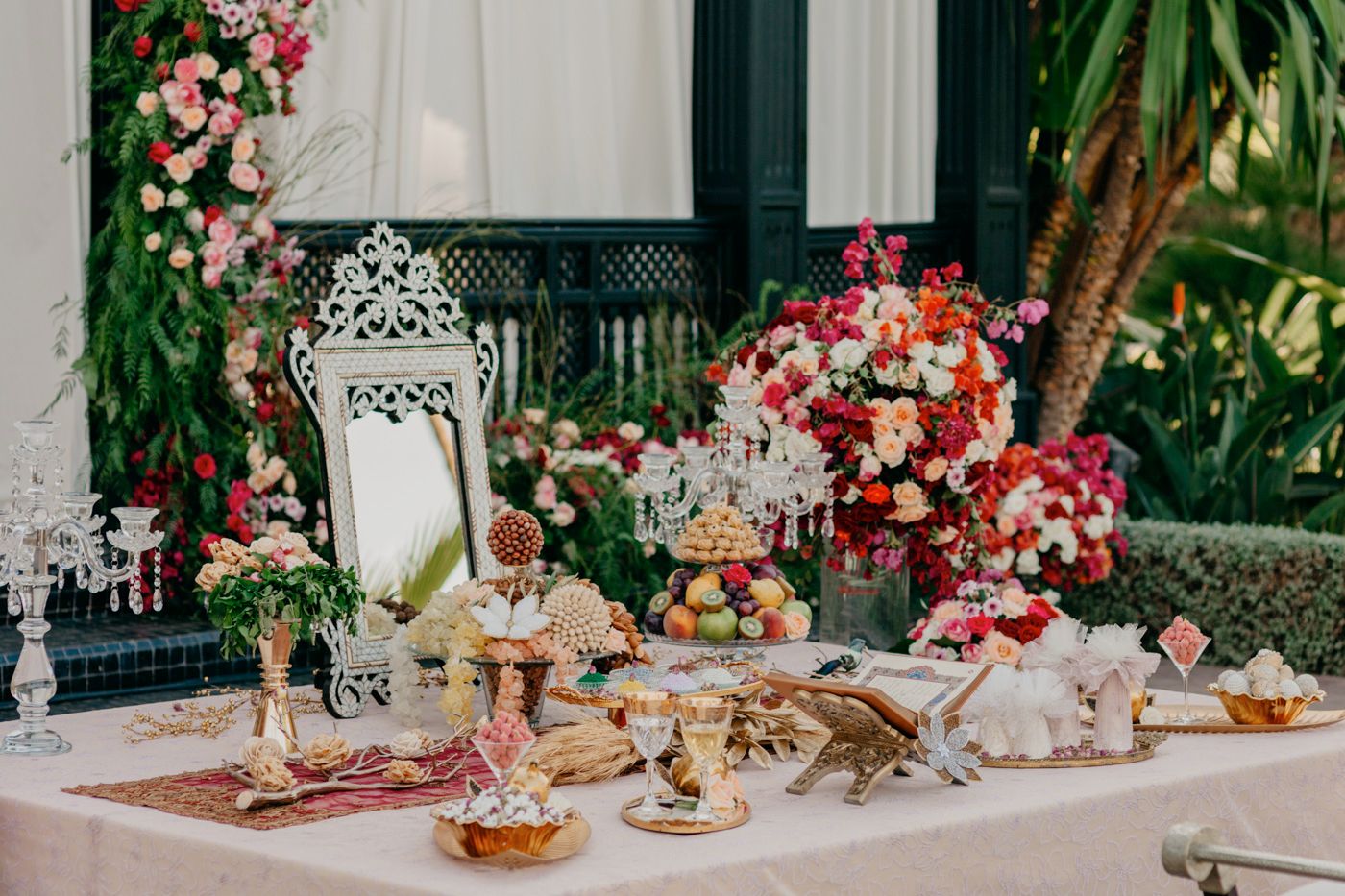 Opulent dessert table decorated with pink flowers, ornate lanterns and delicate pastries.